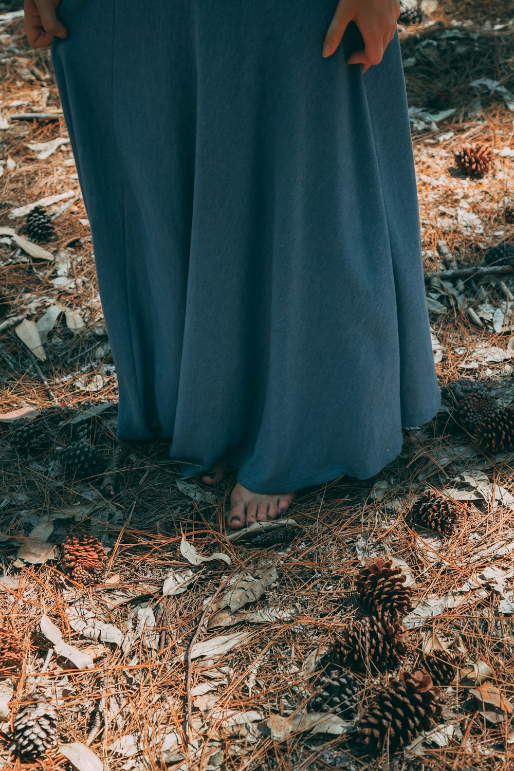 person in gray robe standing on dried leaves