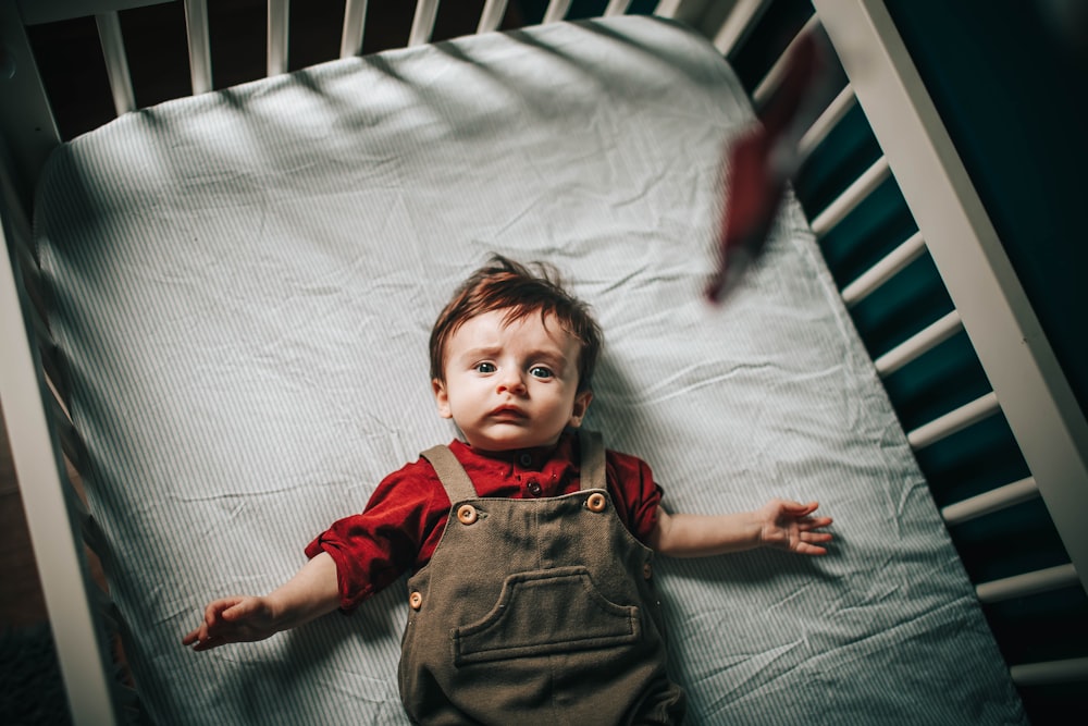 girl in red button up shirt and black denim vest lying on white bed