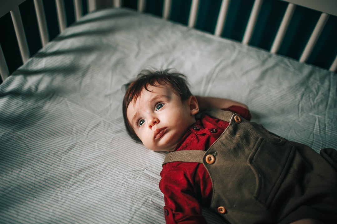 baby in red and gray jacket lying on white bed