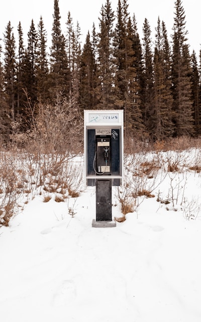 black and gray telephone booth on snow covered ground