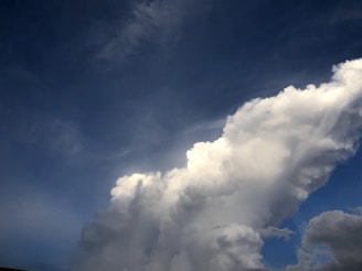 Large, billowing white clouds against a deep blue sky. Wispy details are visible in the cloud formation, suggesting movement and depth.