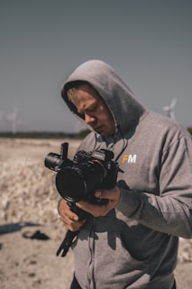 man in gray hoodie holding black nikon dslr camera