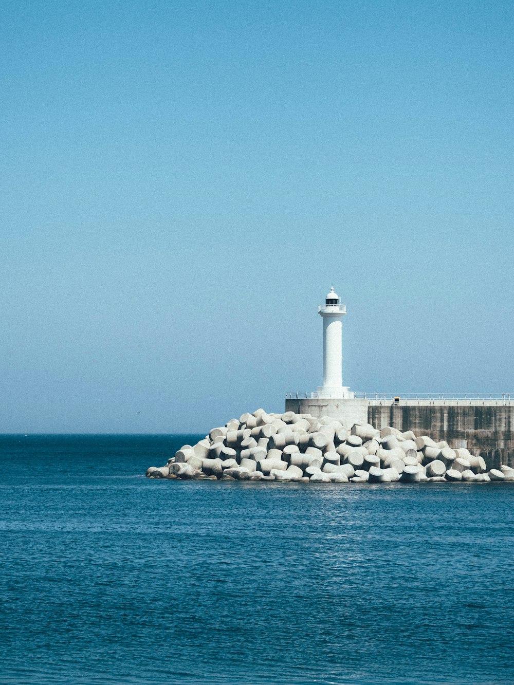 farol branco na formação rochosa cinzenta perto do corpo de água durante o dia