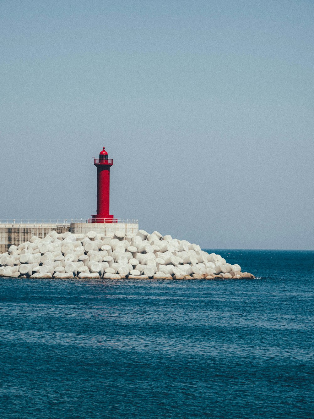 red and white lighthouse on white rock formation near body of water during daytime