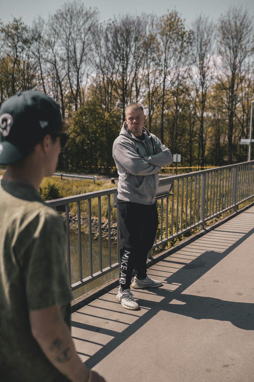 man in gray jacket and black pants standing on bridge during daytime