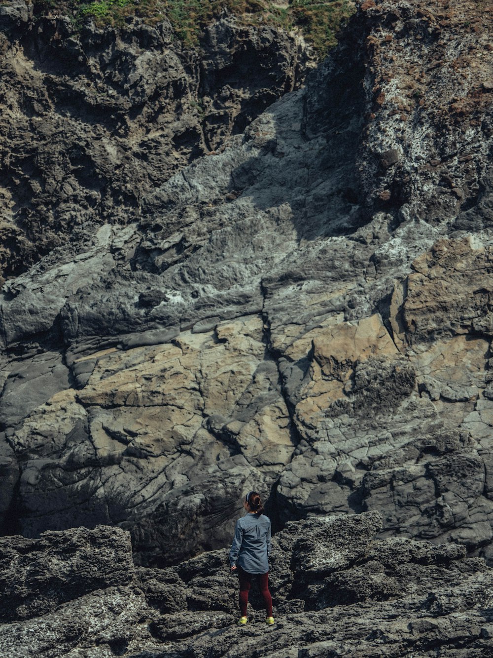 Hombre en chaqueta de mezclilla azul de pie en la montaña rocosa durante el día