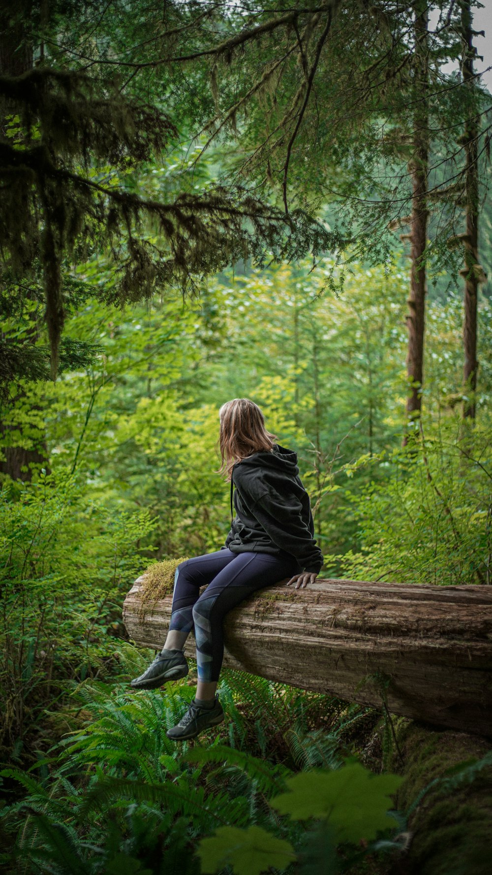 Frau in schwarzem Langarmhemd und blauer Jeans sitzt auf braunem Holzstamm während