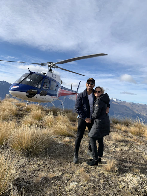 A couple enjoying a private picnic in a quiet mountain meadow, with the helicopter parked nearby.