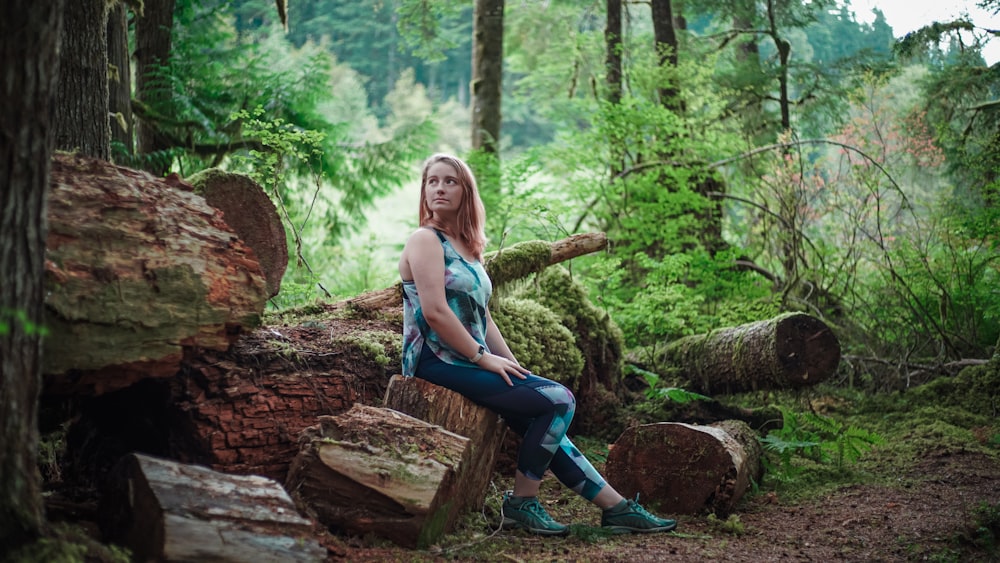 woman in white tank top and blue denim jeans sitting on brown log during daytime