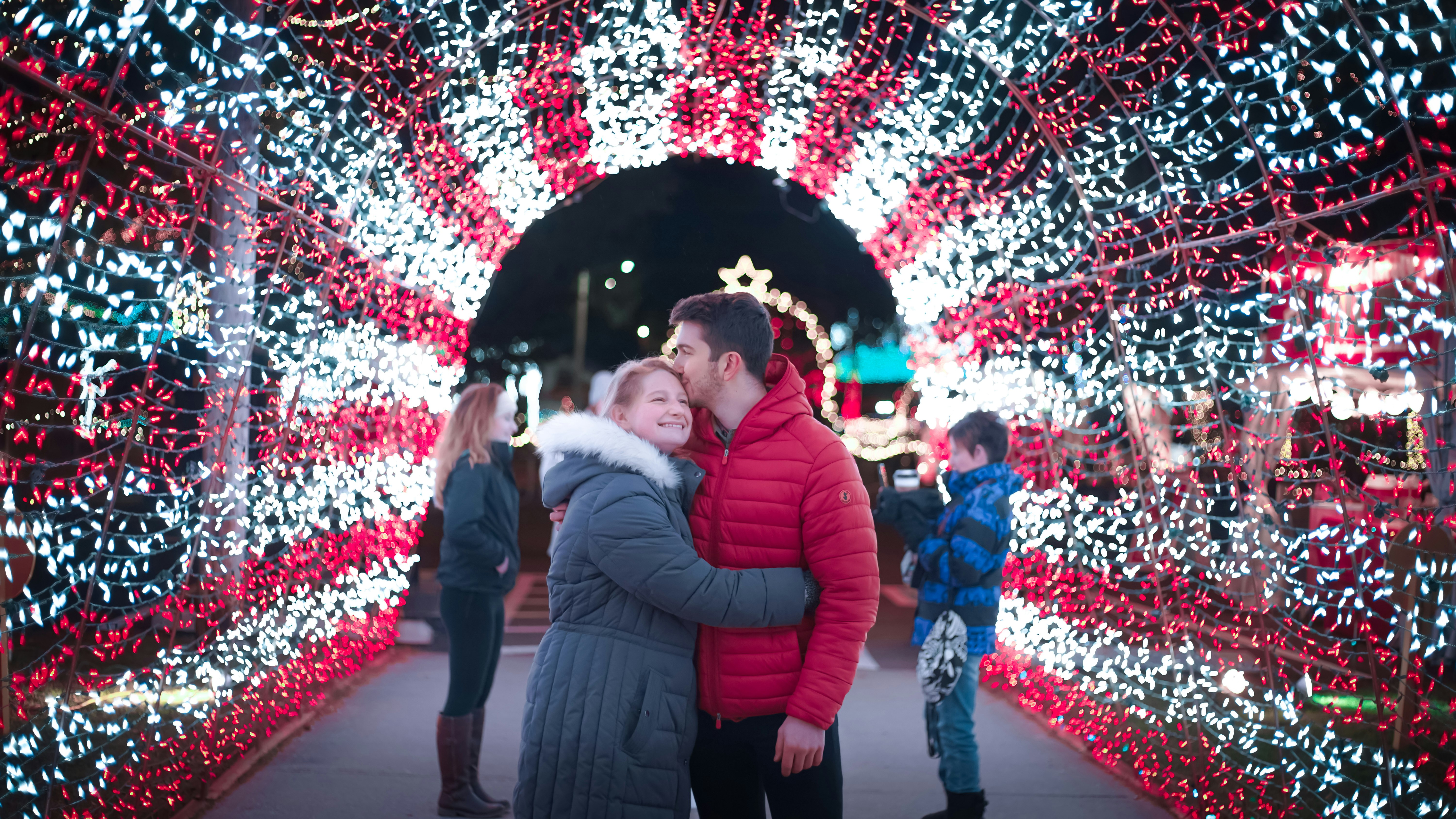 Happy, young couple hugs under holiday lights.