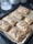 A baking tray filled with freshly baked pastries, likely puff pastries topped with chopped nuts and drizzled icing. They are arranged neatly on parchment paper and have a golden-brown crust.