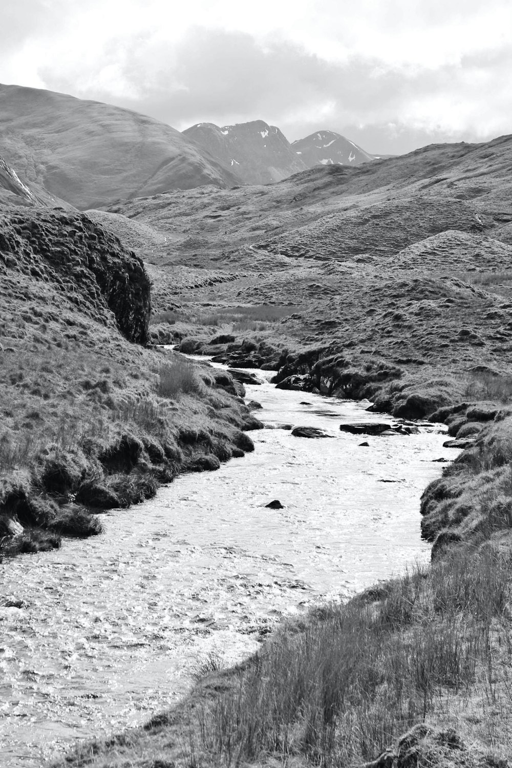 grayscale photo of river between mountains
