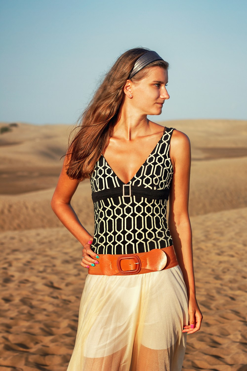 woman in black and white polka dot halter top dress standing on brown sand during daytime