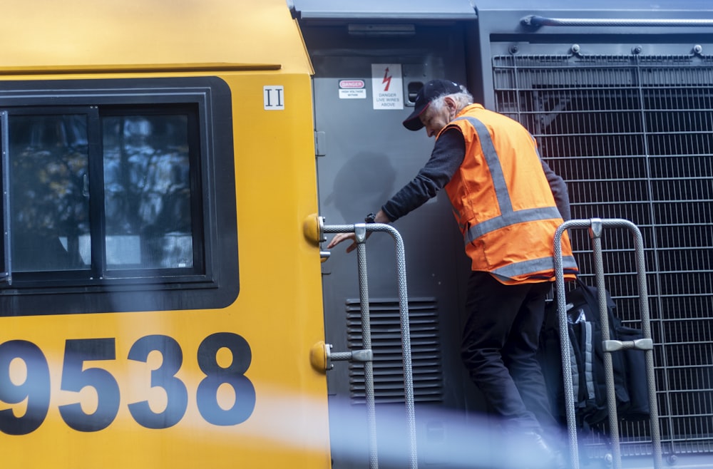 man in orange jacket and black pants standing in front of yellow train