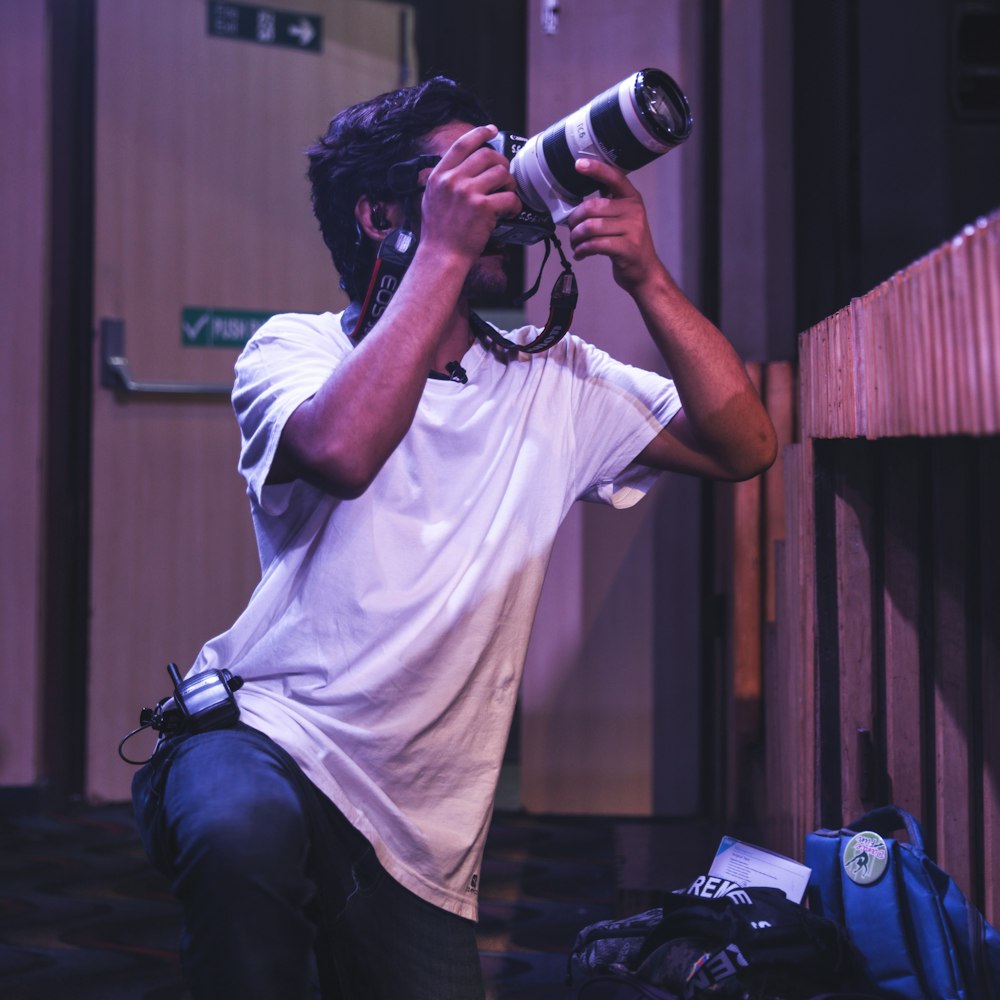 man in white crew neck t-shirt and blue denim jeans holding black dslr camera