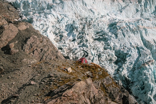 person in red jacket standing on rocky mountain during daytime in Mount Sefton New Zealand