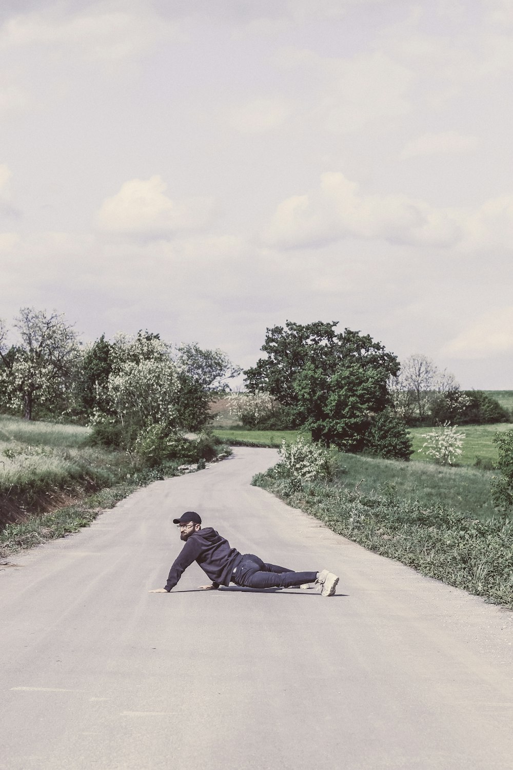 homme en veste noire couché sur une route en béton gris pendant la journée