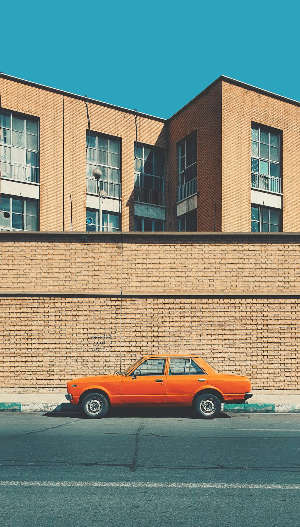 Coche naranja aparcado junto a una pared de ladrillos marrones