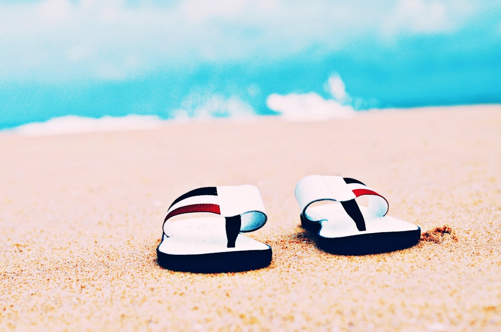 a pair of flip flops sitting on top of a sandy beach