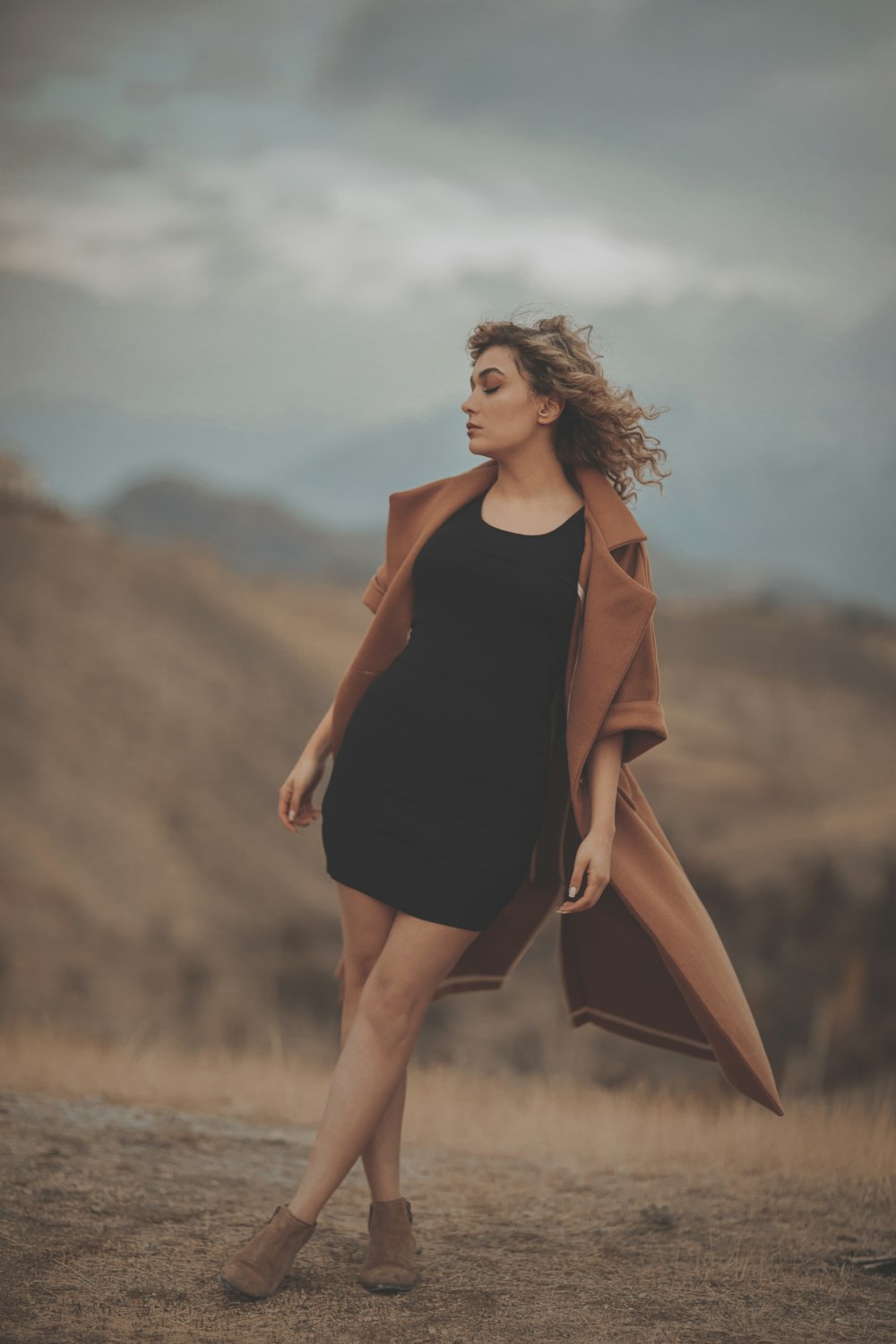 woman in black tank top and brown coat standing on brown grass field during daytime