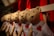 A row of identical plush teddy bears hanging side by side, each wearing a blue and white striped outfit adorned with a red heart on their chest. The background is predominantly red, enhancing the warm ambiance.