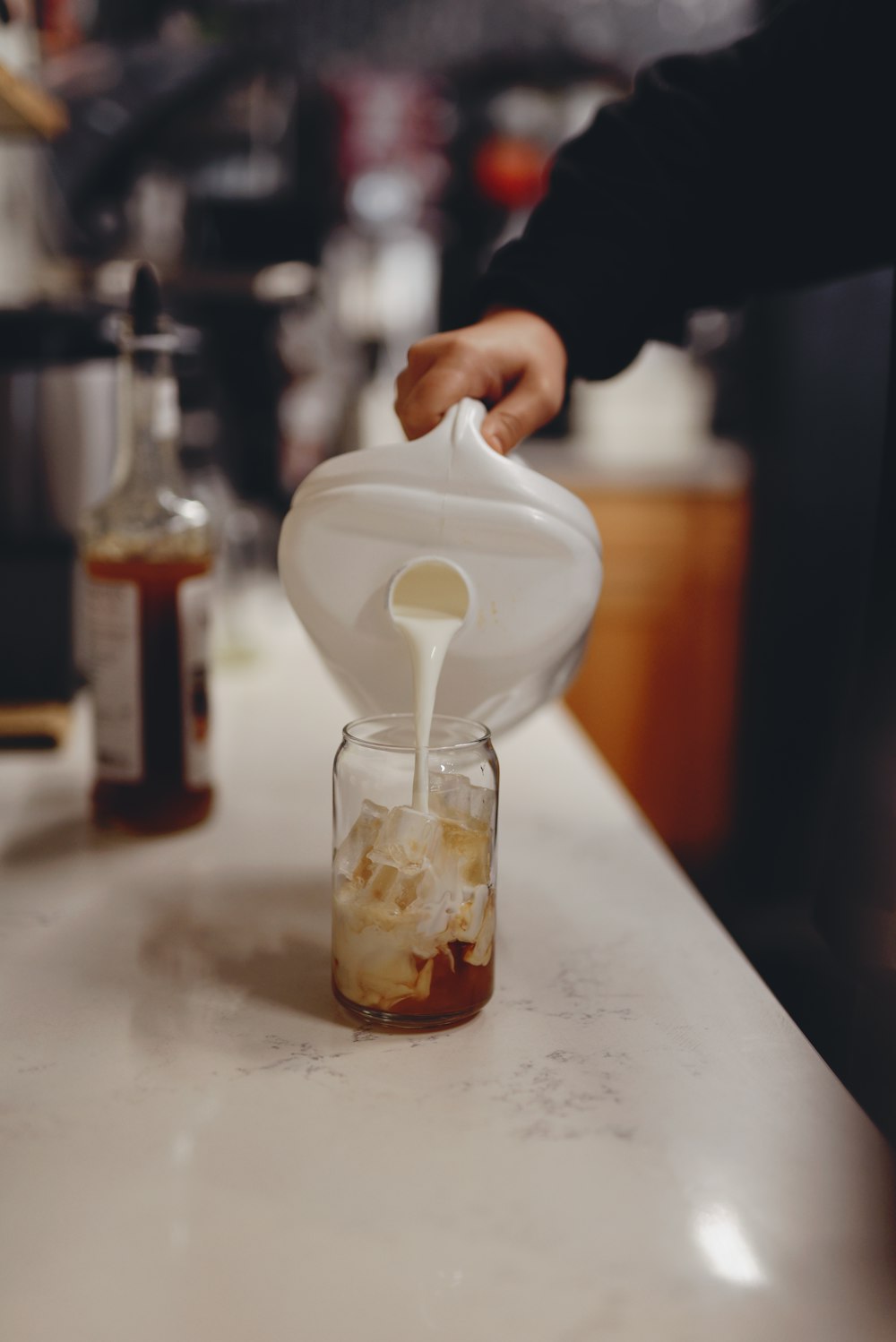 person pouring milk on clear glass jar