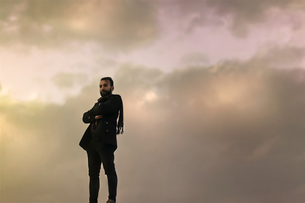 man in black jacket standing under cloudy sky