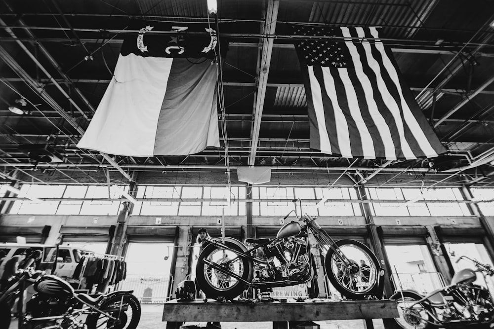grayscale photo of a motorcycle and a flag of us a on a pole
