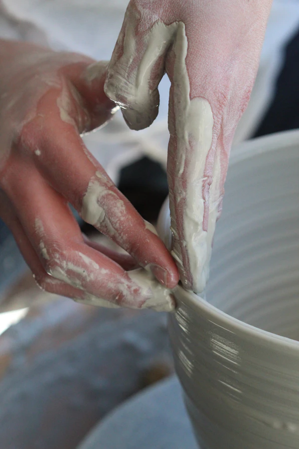 Hands covered in wet clay shaping the rim of a bowl
