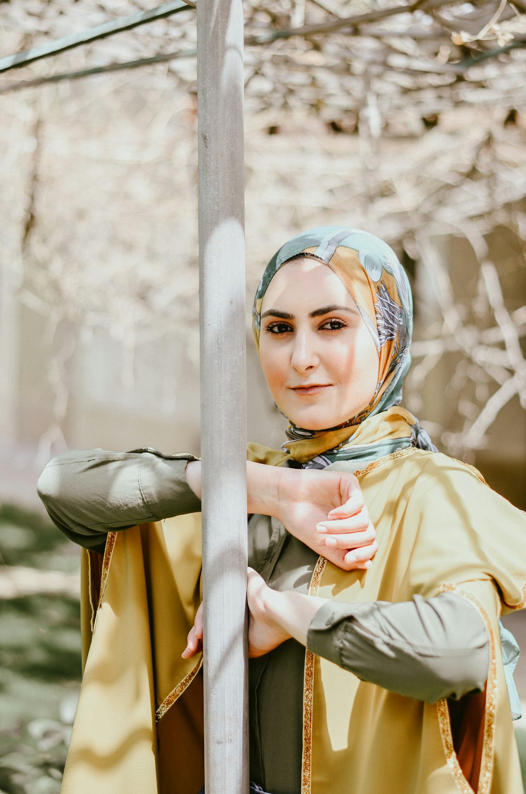 woman in yellow long sleeve shirt and blue and white hijab leaning on gray metal post
