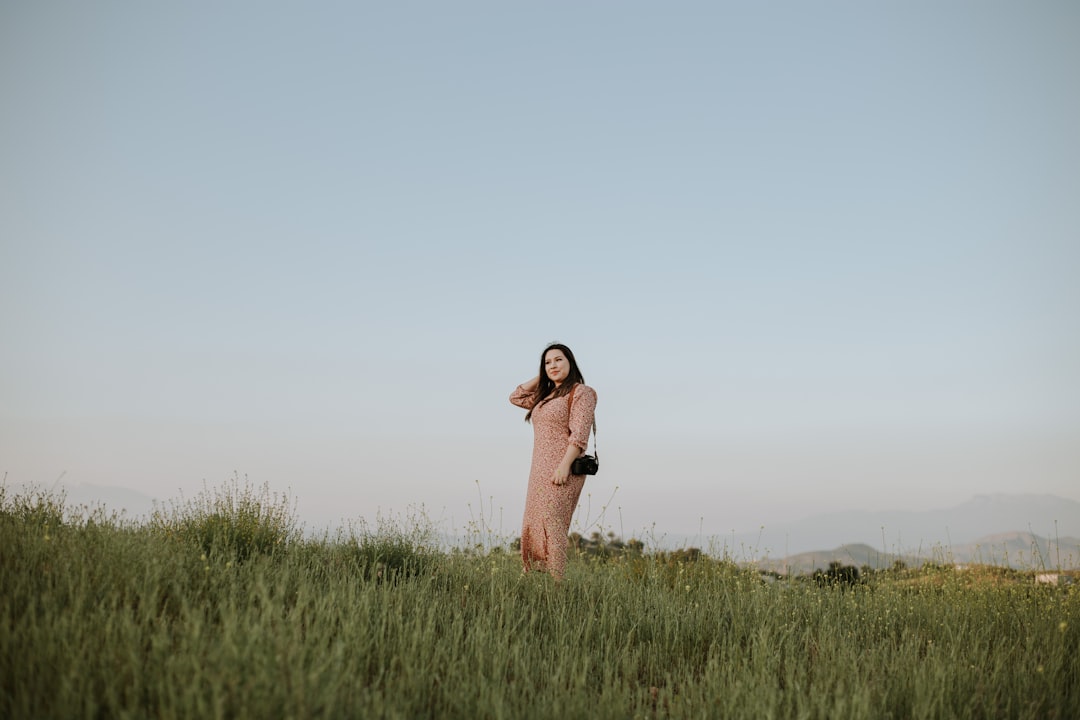 woman in brown coat standing on green grass field during daytime