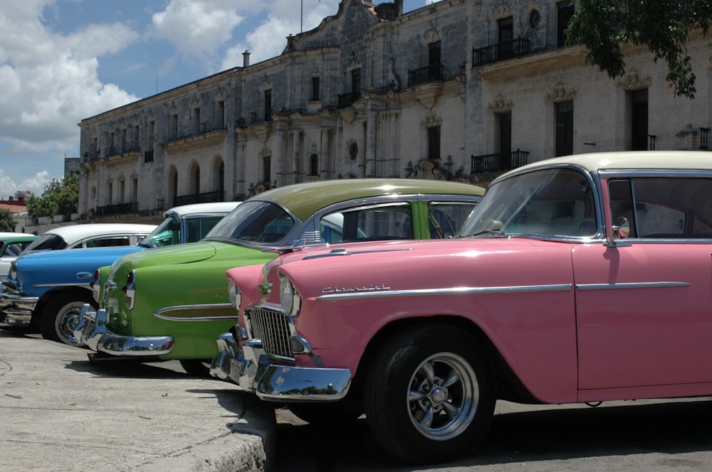 분홍색과 녹색 빈티지 자동차는 낮 동안 갈색 콘크리트 건물 옆에 주차되어 있습니다.
