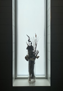 A tall, slender vase with a lustrous glaze and subtle color variations, placed near a sunlit window.