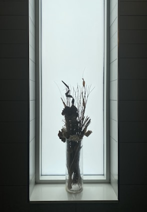 A tall, slender vase with a lustrous glaze and subtle color variations, placed near a sunlit window.