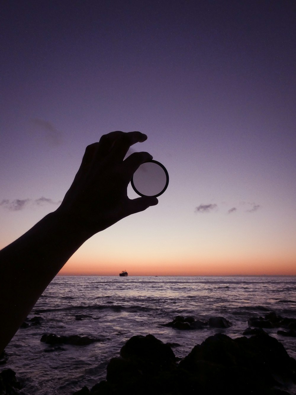 a hand holding a small object over a body of water