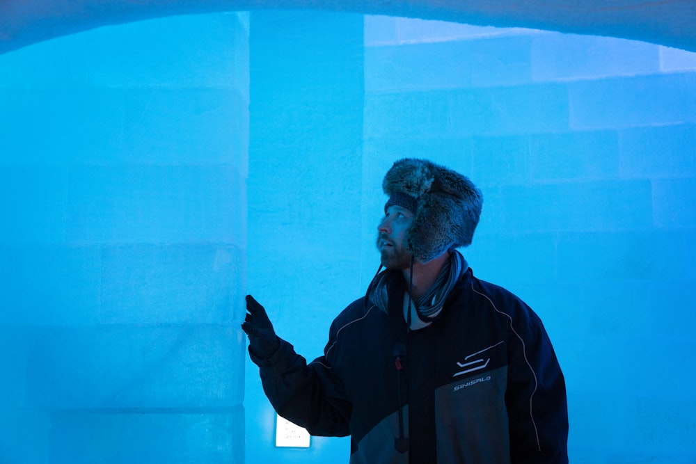 man in black jacket standing near blue wall