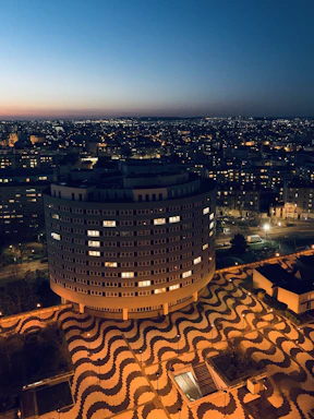 Close-up of hands assembling a detailed cityscape puzzle with bright lights at dusk.