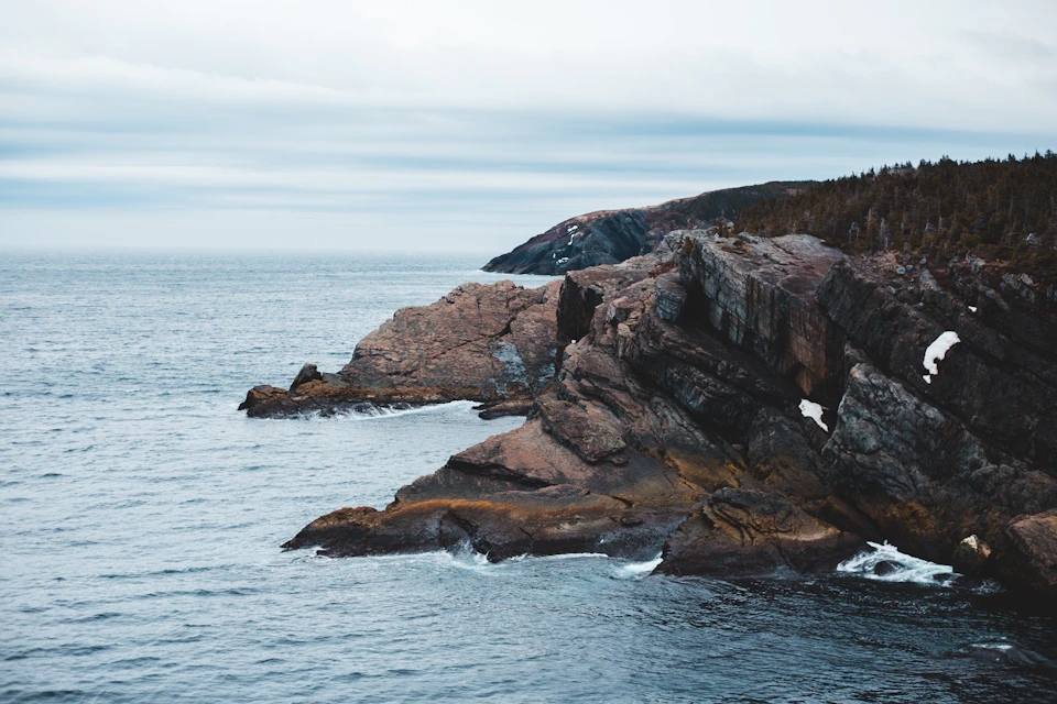 Rocky coastline with large jagged cliff face meets deep blue ocean at horizon line