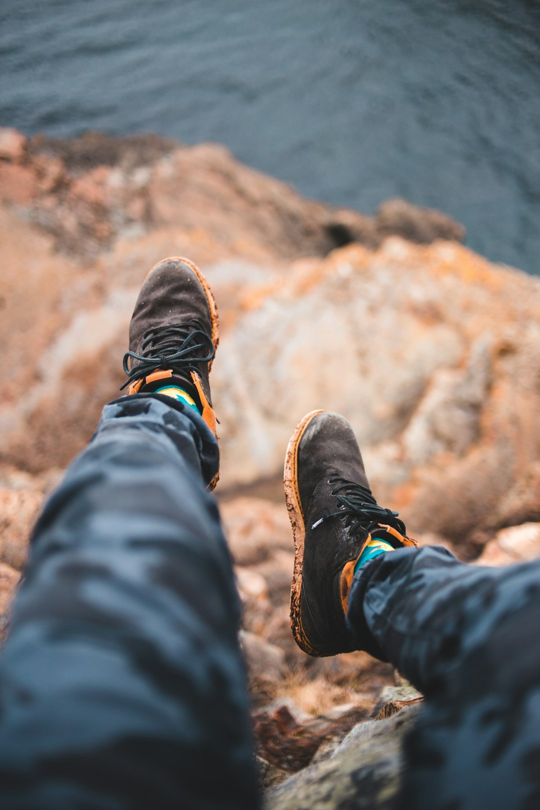 person in black pants and brown hiking shoes sitting on rock during daytime