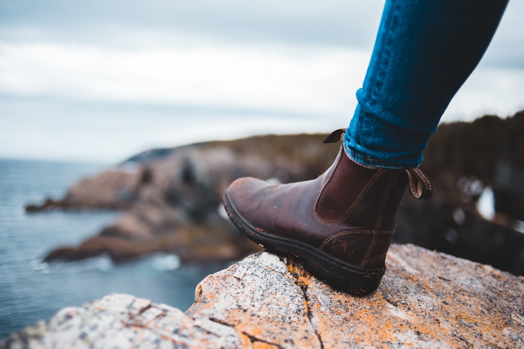 person in blue denim jeans and brown leather shoes standing on rocky shore during daytime