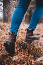 Close-up of a traveler’s boots on a forest trail covered with fallen leaves and moss.