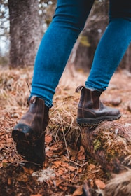 Close-up of a traveler’s boots on a forest trail covered with fallen leaves and moss.