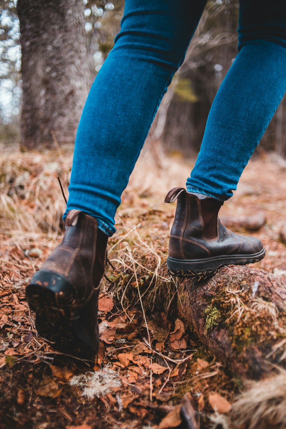 person in blue denim jeans and black leather boots standing on brown dried leaves