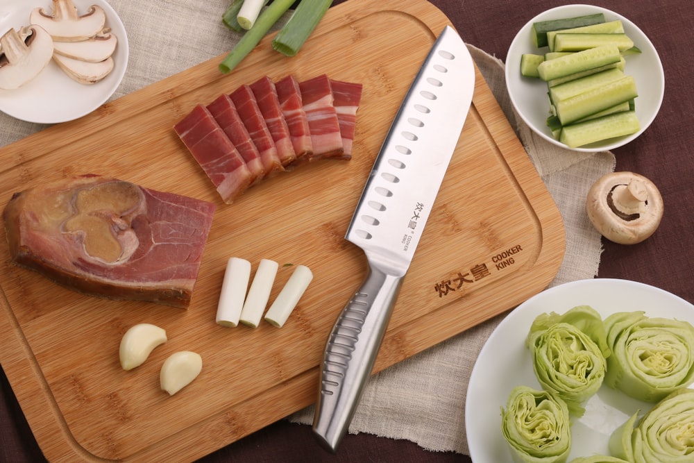 sliced meat on white ceramic plate with silver knife and sliced cucumber