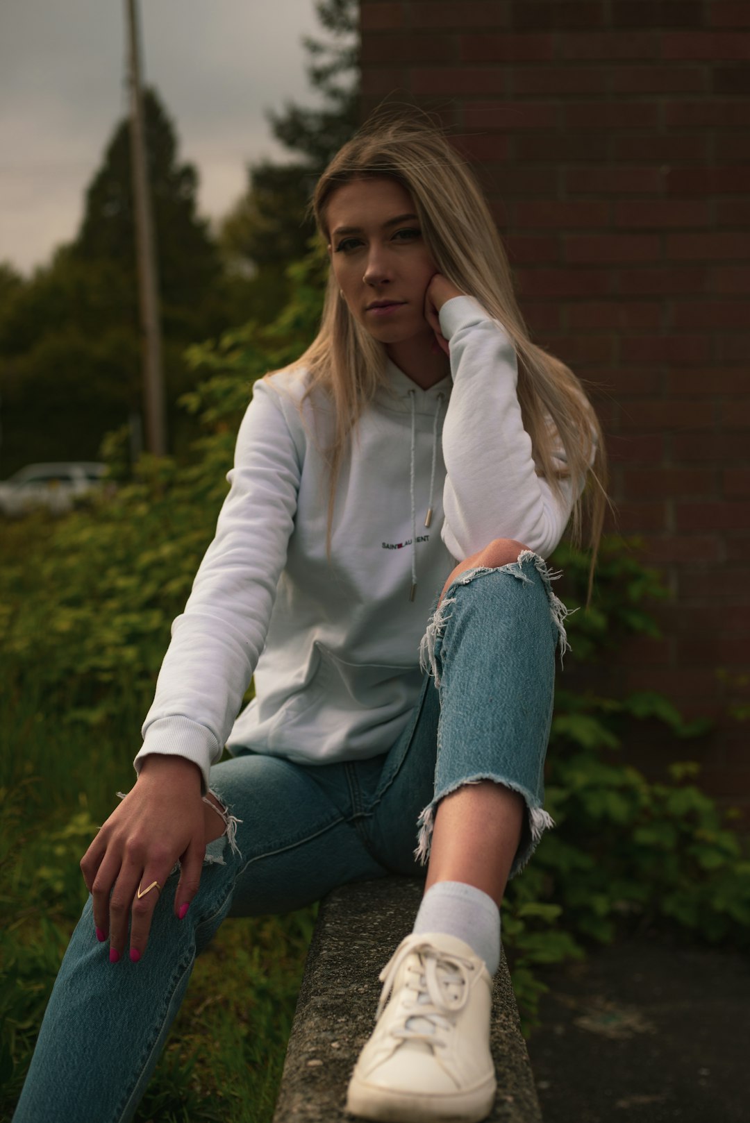 woman in white long sleeve shirt and blue denim jeans sitting on brown concrete brick wall