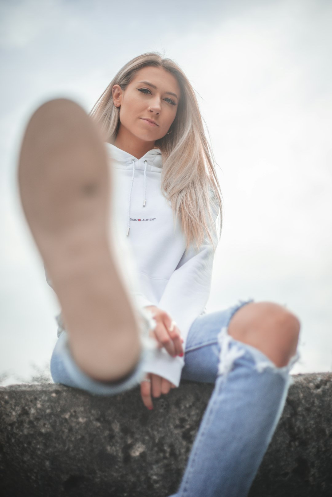 woman in white long sleeve shirt and blue denim jeans sitting on brown rock during daytime