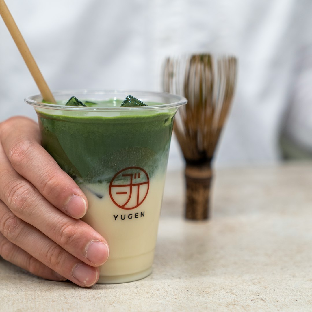 person holding green liquid in white plastic cup