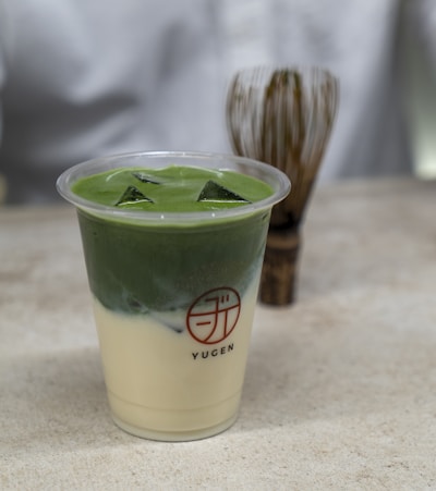 A vibrant matcha drink served in a clear glass with a bamboo whisk.