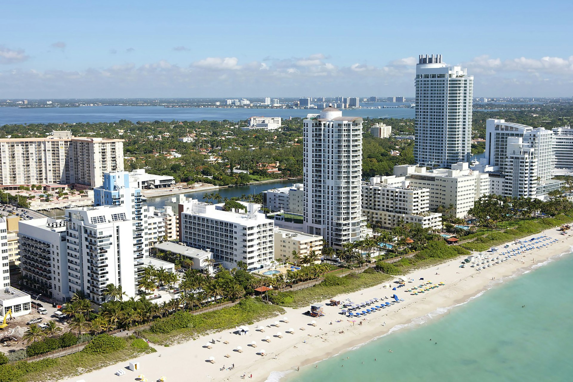 A stunning aerial view of Miami Beach's coastline showing turquoise waters, white sandy beaches, and luxury high-rise condos.