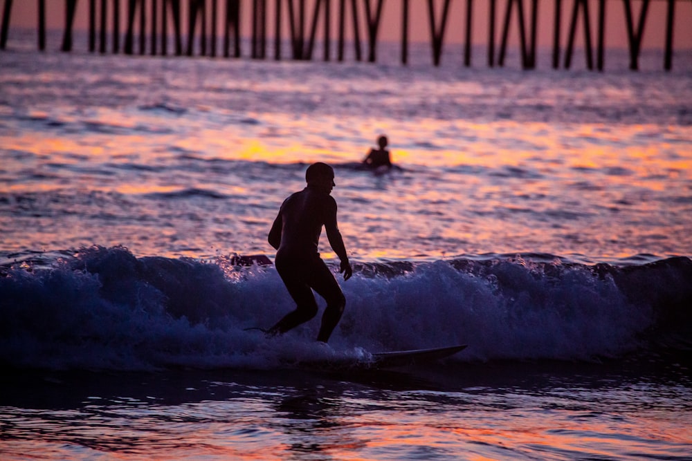 man in black wet suit surfing on sea waves during sunset